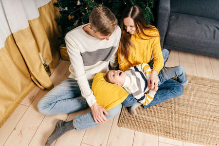 Mom and dad tickle son near the christmas tree. New year game. Top view.の写真素材