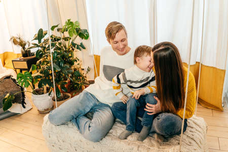 Happy family mother, father and boy have a fun at home in swing. Green houseplants around, sustainable design.の写真素材