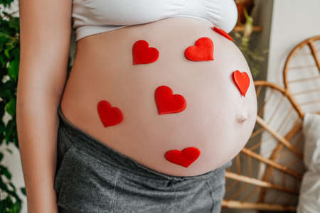 Pregnant woman close-up. Belly with red hearts.