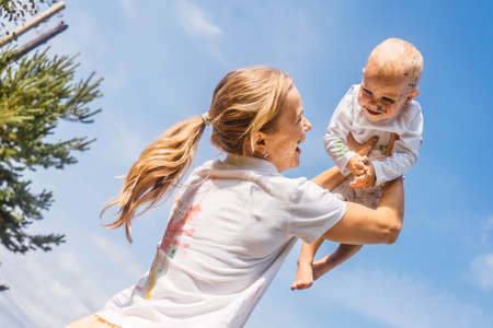 Happy painted mother with baby on sky background. Fun leisure activities with children outdoor.の写真素材