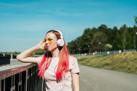 Woman with pink hair in white headphones listening music. Summer time.の写真素材