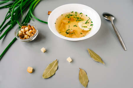Chicken noodle soup with vegetables in a white plate. Spoon, green onion and crackers around plate.の写真素材