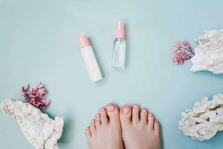 Pink pedicure on blue. Flowers and decorative stones. Cosmetic bottles with oil and cream.の写真素材