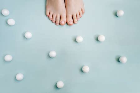 Feet with a pink pedicure on a blue background, little balls around. Copy space.の写真素材