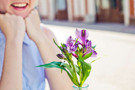 Young smiling woman and purple flowers close-up in summer cafe. Street on background.の写真素材