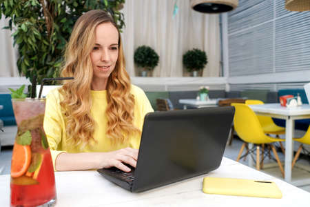 Smiling young female caucasian freelancer is sitting in a street cafe with her netbook.の写真素材