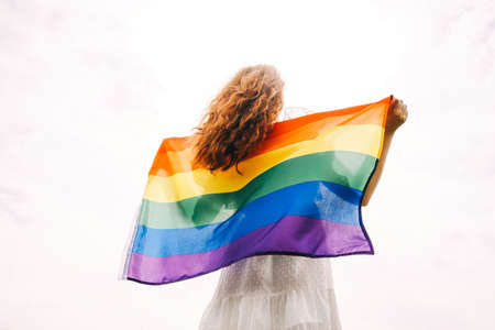 Lesbian woman with rainbow flag on sunny sky background. LGBTQ concept.