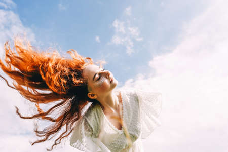 Young happy woman with flying long curly hair in sunshine. Sky background. Copy space.の写真素材