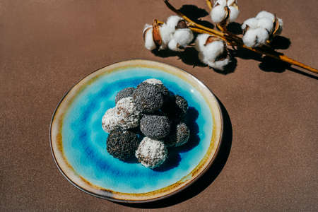 Homemade date candies covered with poppy, sesame and shredded coconut. Blue plate on brown...