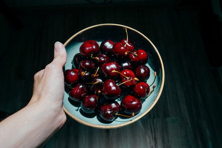 Cherries in a bowl in hand on black background. Sunny day.