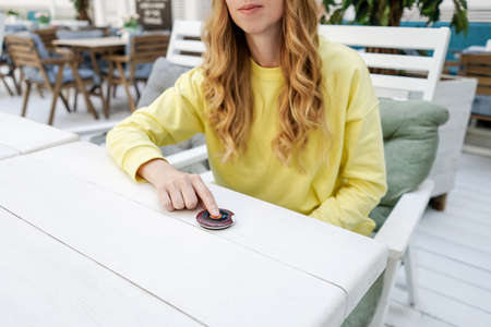 A young woman presses the button to call the waiter in a summer cafe.