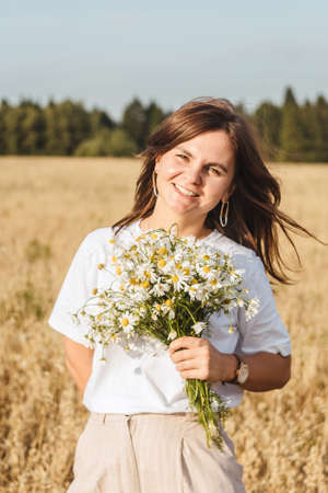 Portrait of the young beautiful smiling woman outdoors in field. Close-up, bouquet chamomile in hands.の写真素材