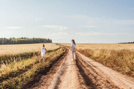 Beautiful young mother and her daughter having fun at the country road. White clothes, freedom concept.の写真素材