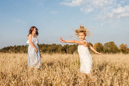 Beautiful young mother and her daughter dance in field. White clothes, freedom concept. Front view.の写真素材
