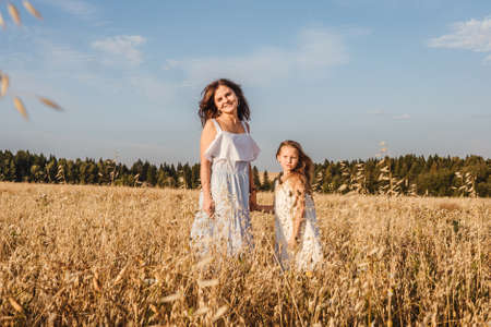 Beautiful young mother and her daughter dance in field. White clothes, freedom concept. Front view.の写真素材