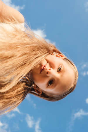 Portrait of little girl outdoor, bottom view, close-up. Blue sky background.の写真素材