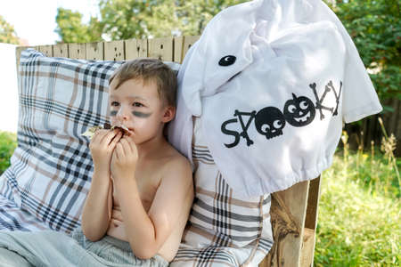 Cute Little Boy eat Halloween candy outdoor. Ghost costume near boy, after trick or treat.の写真素材