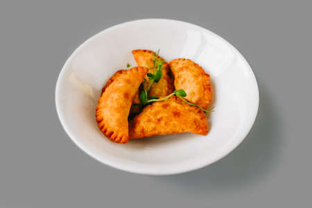 Fried pies on a white plate on gray background. Russian tea time. Front view.