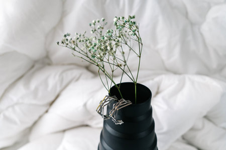 Imitation jewelry, silver bijouterie earrings on black vase. White textile backgroundの写真素材