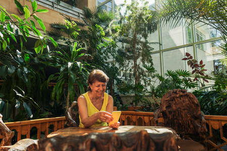 Senior Woman use phone in botanical garden. Green plants around, sustainable design.の写真素材