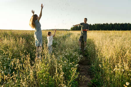 Mother, father and child son having fun in field on sunset. Man blowing bubbles.の写真素材