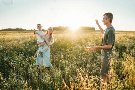 Mother, father and child son having fun in field on sunset. Man blowing bubbles.の写真素材