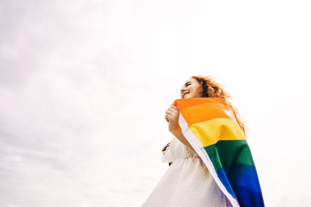 Lesbian woman with rainbow flag on sunny sky background. LGBTQ concept.の写真素材