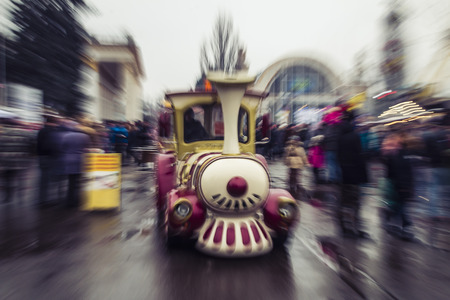 New Year's children's train on the square at the festival among people in the effect of blurring and...