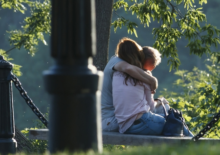 a loving couple hugging in a green park on a warm sunny day on a bench back view