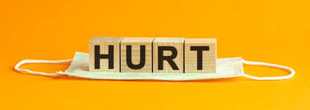 Wooden block with words HURT on wooden cubes, with the medical mask , health concept, yellow background.の写真素材