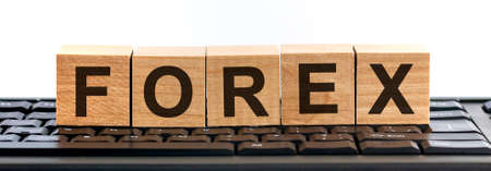 FOREX word made with building blocks. A row of wooden cubes with a word written in black font is located on a keyboard.の写真素材