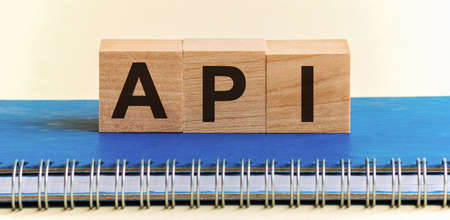 API - a word made of wooden blocks with black letters, a row of blocks is located on a blue Notepad. White background, front view. Api code, promo code concept.の写真素材
