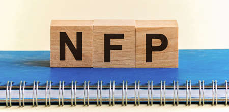 Wooden blocks with the word NFP. Nonfarm Payrolls - key economic indicator. NFP - a word made of wooden blocks with black letters, a row of blocks is located on a blue Notepad. White background, front view. Promotion code, promo code concept.の写真素材
