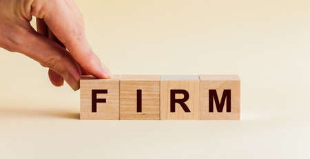The hand puts a wooden cube with the letter F from the word FIRM. The word is written on wooden...