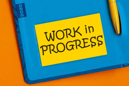 Yellow paper for notes with text Work In Progress on the office background.の写真素材