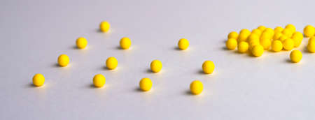 Keep your distance. Round yellow tablets are scattered at a distance on a white glossy table on top....
