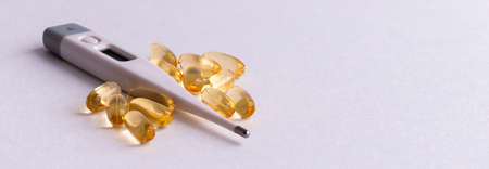 Medical digital thermometer with pills and vitamins on a white background.