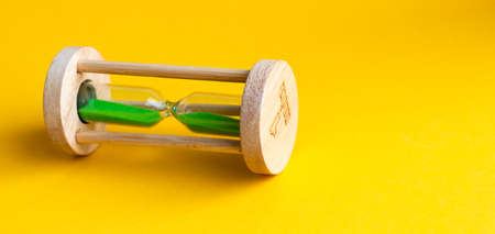 Hourglass with green sand inside on a yellow background.