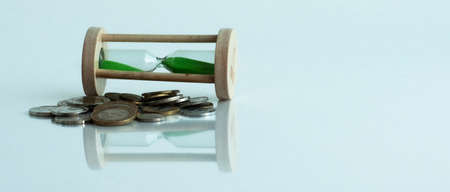 hourglass and coins on a white background and reflection in a mirror surface.