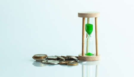 hourglass and coins on a white background and reflection in a mirror surface.