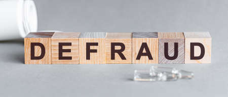 Defraud is a word written in black letters on wooden cubes, gray bsckground.の写真素材
