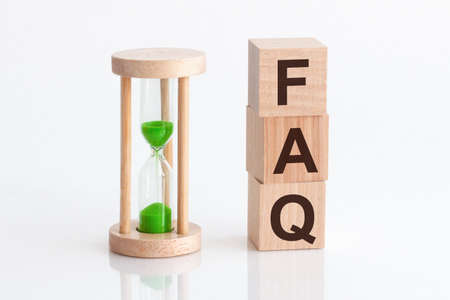 Close-up of an hourglass next to wooden blocks with the text FAQ - Frequently Asked Question. FAQ white backgrounds.の写真素材