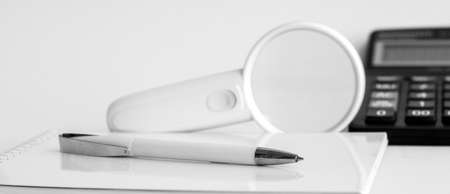 A white magnifying glass and a white pen are on the Notepad. In the background is a calculatorの写真素材