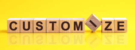 customize word written on wood block. customize word is made of wooden building blocks lying on the yellow table. customize, business concept, yellow backgroundの写真素材