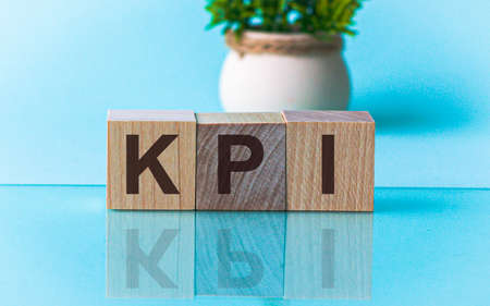 Word KPI made with wood building blocks, stock image. he written text is mirrored from the glossy surface. In the background is a flower in a pot.の写真素材