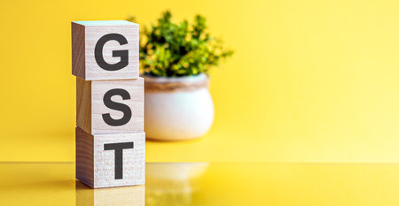 Motivational words: GST in 3d wooden alphabet letters on a bright yellow background with copy space, business concept. GST - Goods and Services Tax.の写真素材