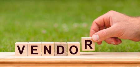 Word Vendor written with wooden blocks. Man hand holding wooden cube block with Vendor - business word on green lawn background.の写真素材