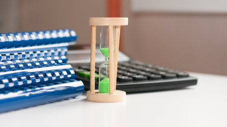 Black calculator and hourglass with green sand close-up stand on a white wooden table, business environment of the workplaceの写真素材