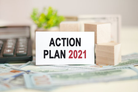ACTION PLAN 2021 text on white paper, on the background of money bills, banknotes and wooden blocks,...