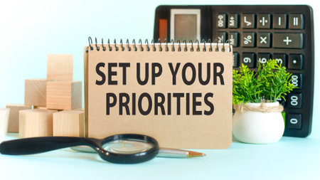 Business concept. Notebook with text Set up your priorities sheet of white paper for notes, calculator, magnifying glass, woden blocks, on the charts backgroundの写真素材